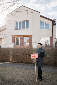 Woman Standing by For Sale Banner by House